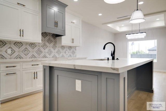 kitchen featuring sink, light hardwood / wood-style flooring, an island with sink, a tray ceiling, and decorative light fixtures