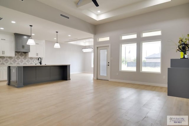 kitchen with white cabinets, an island with sink, hanging light fixtures, and light wood-type flooring