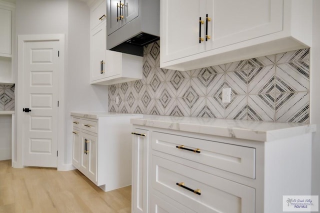 kitchen with white cabinetry, backsplash, light stone counters, and light wood-type flooring