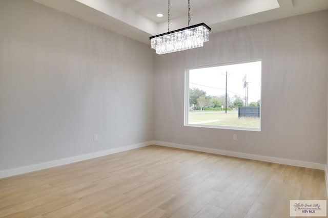 empty room with a raised ceiling, an inviting chandelier, and light hardwood / wood-style flooring