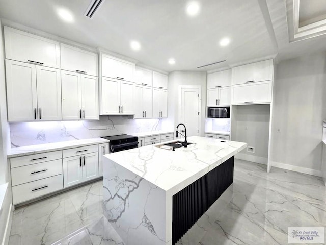 121 Finch Dr, Los Fresnos, TX 78566 - kitchen with stainless steel microwave, light marble finish flooring, recessed lighting, white cabinetry, and a kitchen island with sink