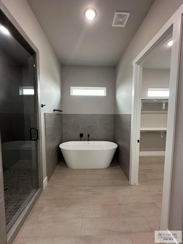 bathroom with tile walls, shower with separate bathtub, and wood-type flooring