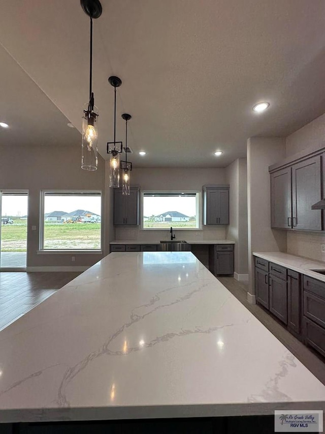 kitchen featuring a spacious island, decorative light fixtures, sink, gray cabinets, and light stone counters