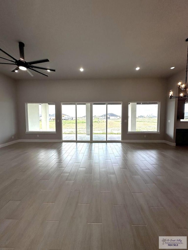 unfurnished living room with ceiling fan with notable chandelier and wood-type flooring