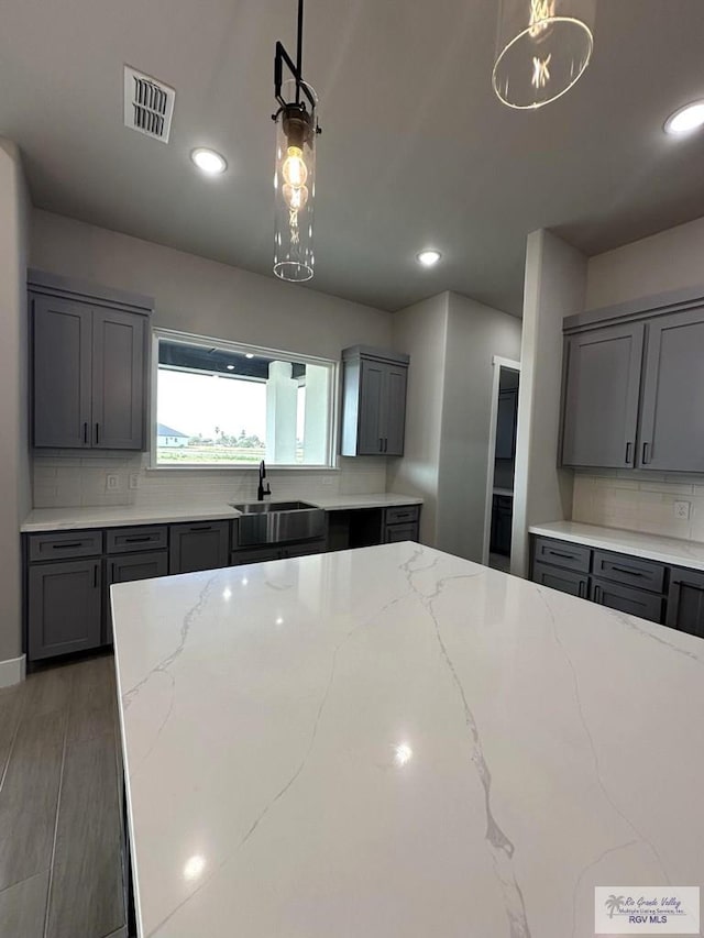 kitchen featuring gray cabinets, tasteful backsplash, light stone counters, and pendant lighting