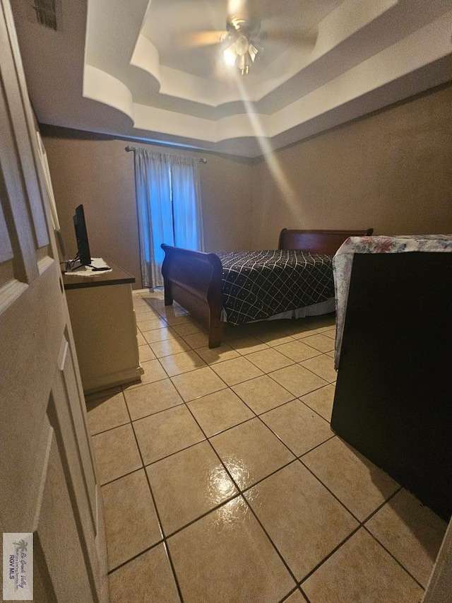 bedroom featuring ceiling fan, light tile patterned floors, and a tray ceiling