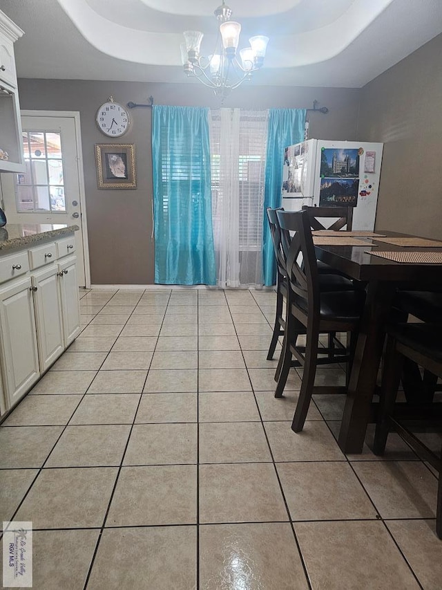 tiled dining room with a tray ceiling and a notable chandelier