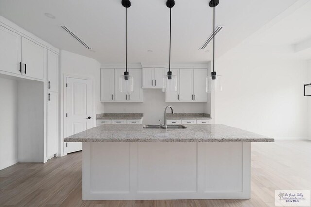 kitchen with hanging light fixtures, white cabinetry, a kitchen island with sink, and sink