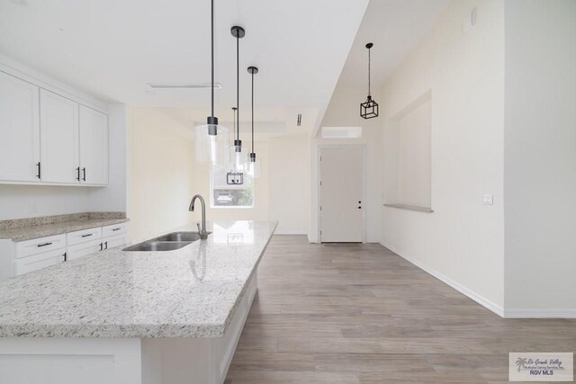 kitchen with white cabinetry, an island with sink, pendant lighting, and light wood-type flooring