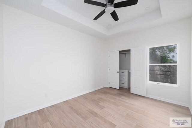 unfurnished bedroom with a closet, light wood-type flooring, a tray ceiling, and ceiling fan