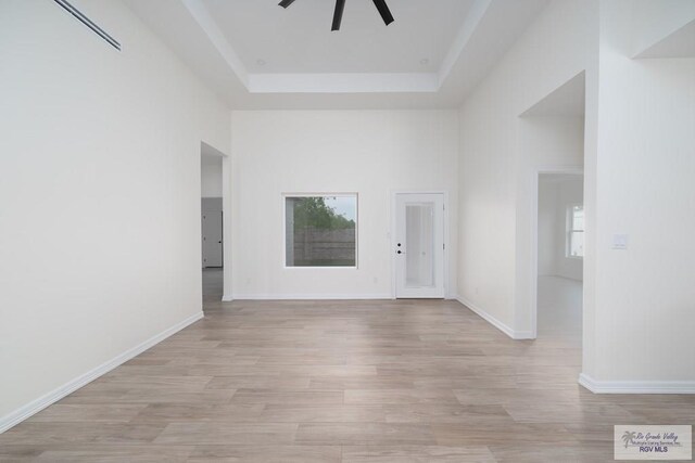 unfurnished room with light wood-type flooring, a raised ceiling, and ceiling fan