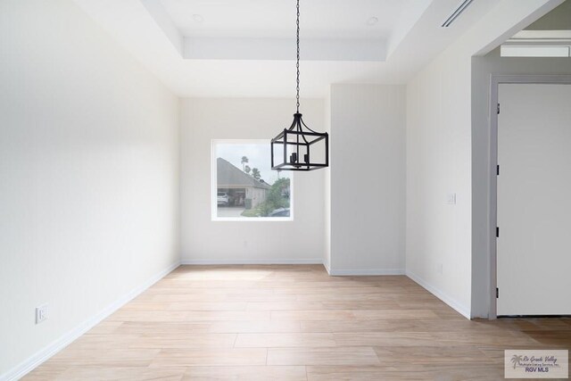 unfurnished dining area featuring a tray ceiling, a chandelier, and light wood-type flooring