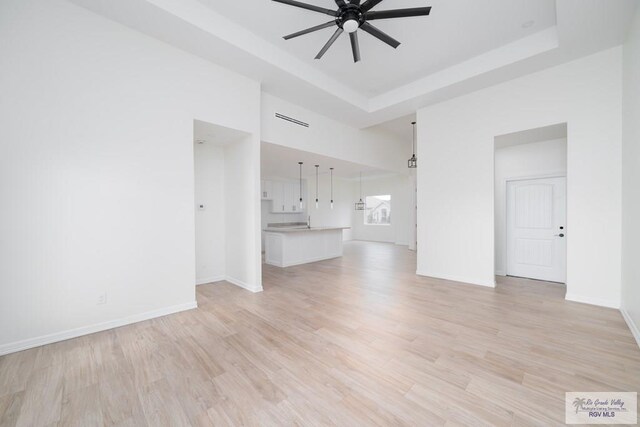 unfurnished room featuring ceiling fan, a raised ceiling, and light hardwood / wood-style flooring