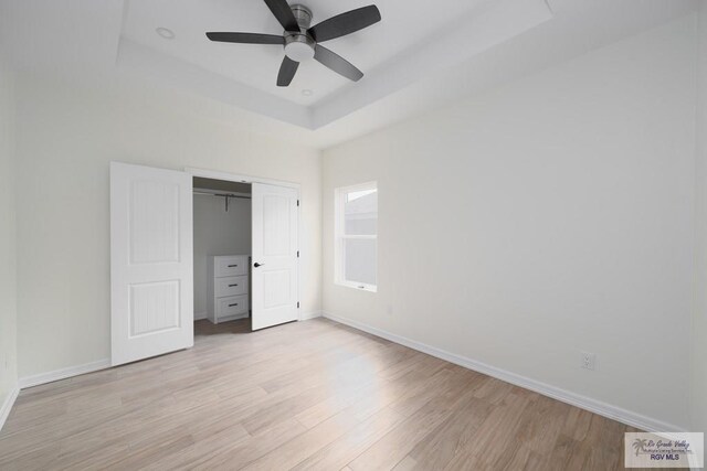 unfurnished bedroom featuring a raised ceiling, ceiling fan, a closet, and light hardwood / wood-style floors