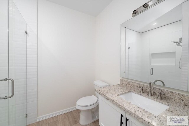 bathroom with hardwood / wood-style floors, vanity, toilet, and walk in shower