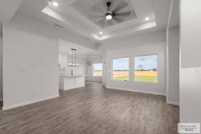unfurnished living room with dark wood-style flooring, ceiling fan, a raised ceiling, and baseboards
