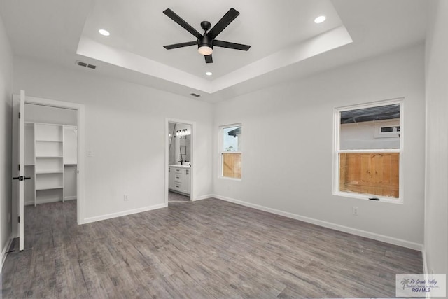 unfurnished bedroom featuring recessed lighting, a spacious closet, wood finished floors, visible vents, and a tray ceiling