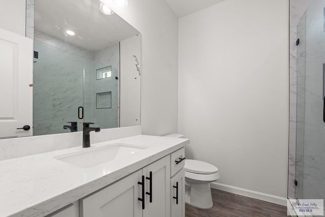 bathroom featuring vanity, toilet, a marble finish shower, baseboards, and wood finished floors