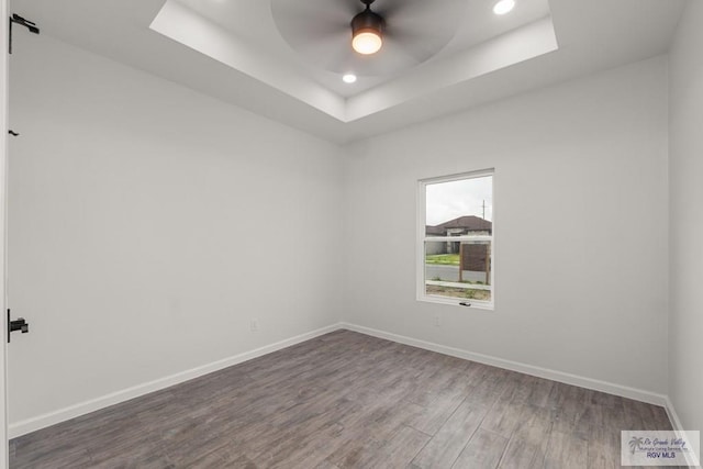 spare room with a tray ceiling, baseboards, recessed lighting, wood finished floors, and a ceiling fan