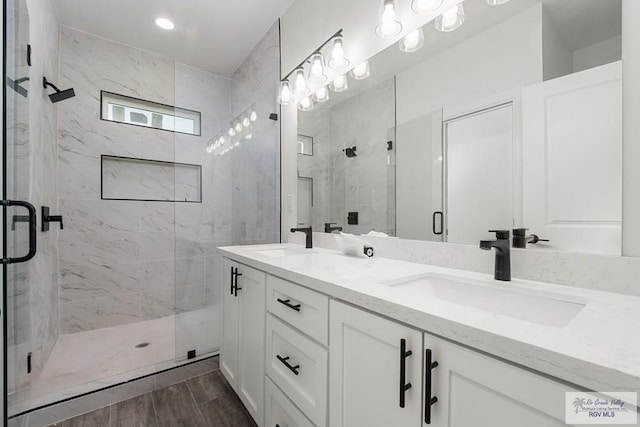 bathroom with double vanity, a marble finish shower, and a sink