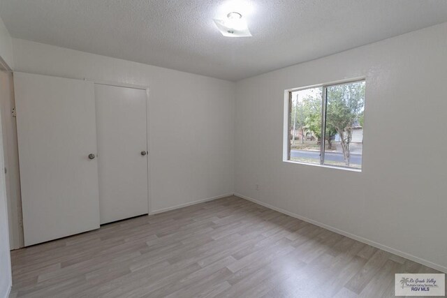225 Chelo Dr, La Feria, TX 78559 - unfurnished bedroom featuring baseboards, light wood finished floors, and a textured ceiling