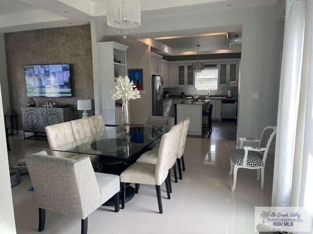 tiled dining space with sink, a tray ceiling, and a notable chandelier