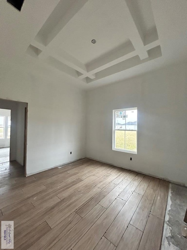 spare room featuring a healthy amount of sunlight, coffered ceiling, and light hardwood / wood-style floors