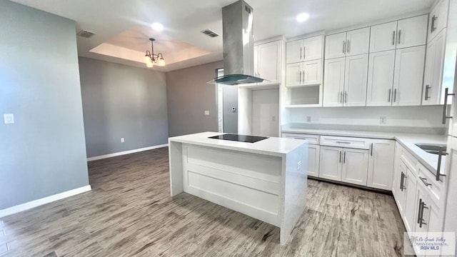 kitchen featuring island exhaust hood, black electric stovetop, a tray ceiling, light hardwood / wood-style floors, and white cabinetry