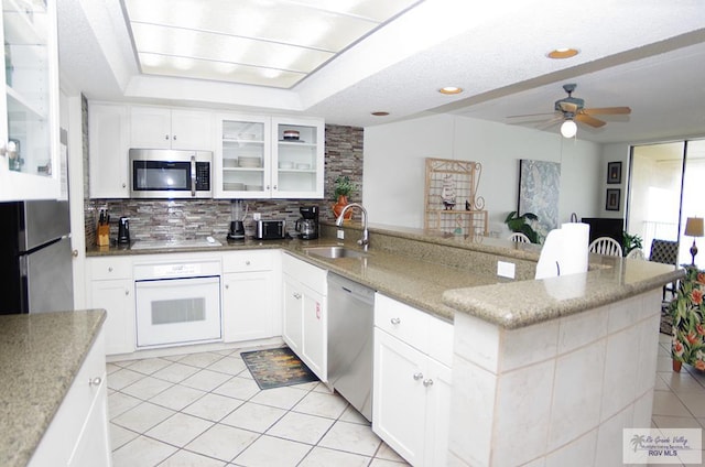 kitchen with appliances with stainless steel finishes, backsplash, light stone counters, sink, and white cabinets