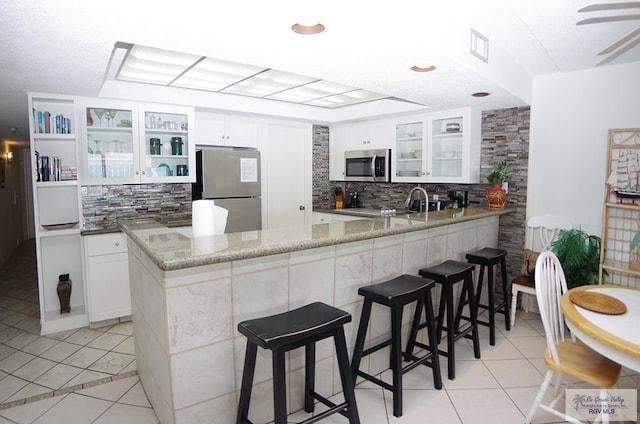 kitchen featuring white cabinetry, stainless steel appliances, light stone counters, kitchen peninsula, and light tile patterned floors