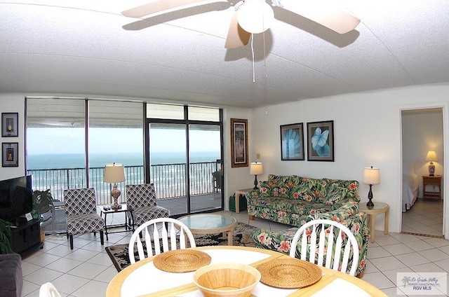 tiled living room with ceiling fan, a water view, and a textured ceiling