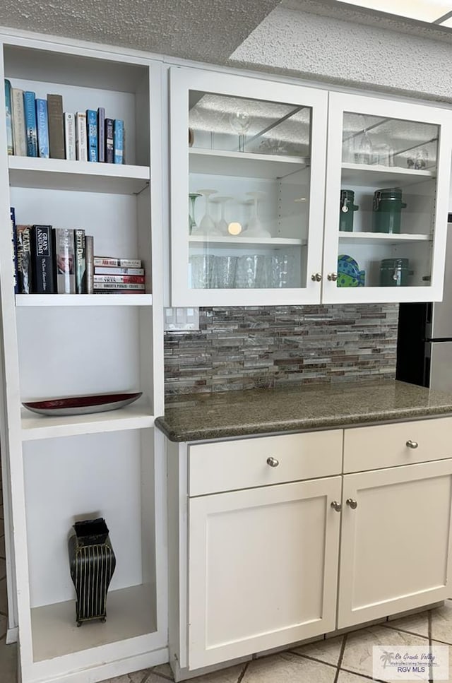 bar featuring light tile patterned flooring, dark stone countertops, white cabinetry, and backsplash