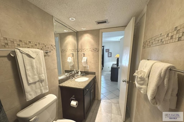 bathroom with a textured ceiling, tile patterned flooring, and tile walls