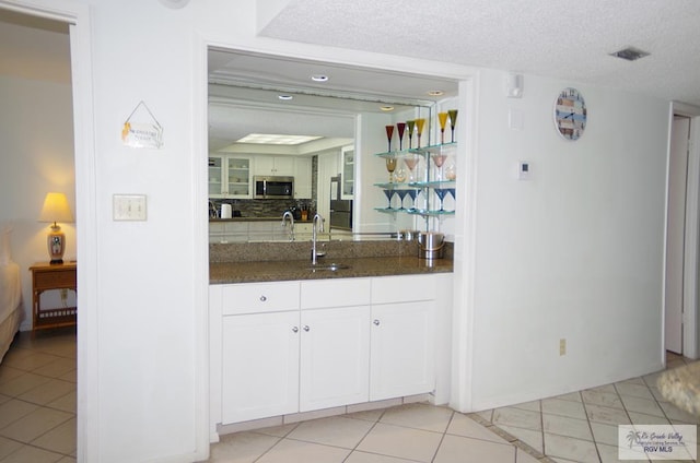 kitchen featuring backsplash, a textured ceiling, sink, light tile patterned floors, and white cabinetry