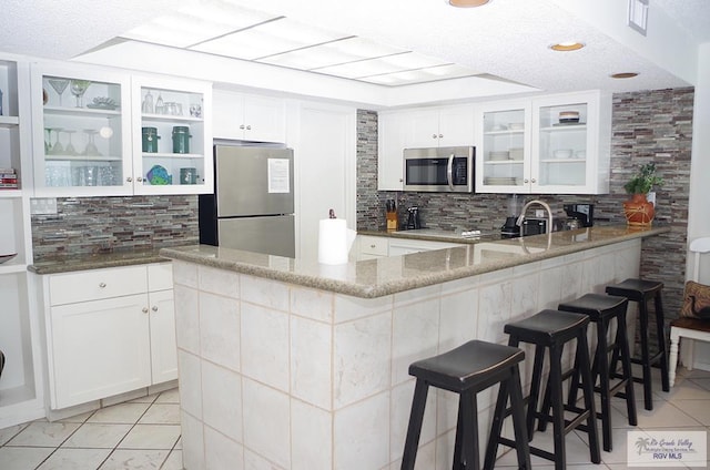 kitchen featuring light stone countertops, appliances with stainless steel finishes, a kitchen breakfast bar, a textured ceiling, and white cabinets