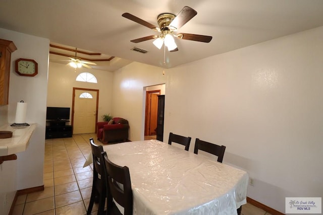 tiled dining room with ceiling fan and a raised ceiling