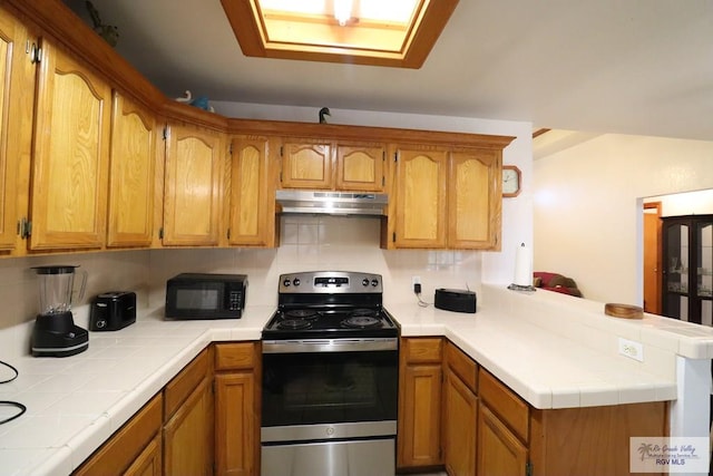 kitchen featuring kitchen peninsula, stainless steel electric range oven, tile countertops, and tasteful backsplash