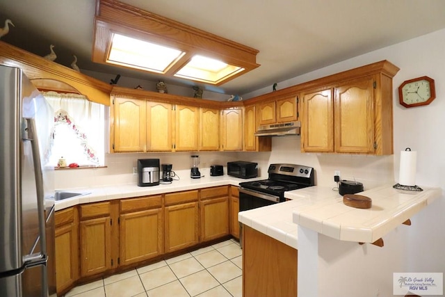 kitchen with light tile patterned floors, appliances with stainless steel finishes, kitchen peninsula, and tile countertops