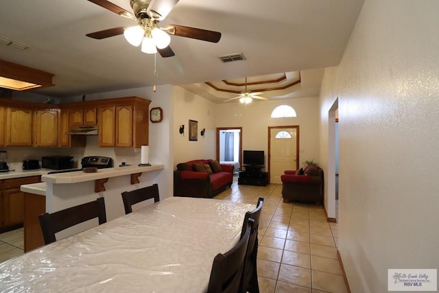 dining area with ceiling fan, light tile patterned flooring, and a tray ceiling