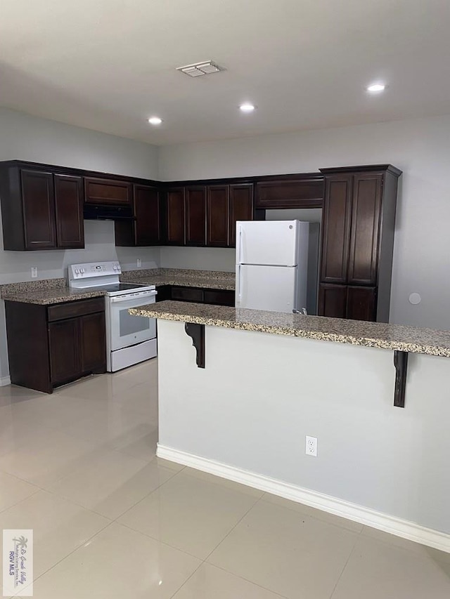 kitchen with dark brown cabinets, white appliances, a breakfast bar area, and light tile patterned floors