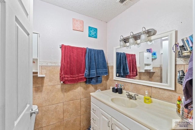 bathroom with visible vents, a textured ceiling, tile walls, wainscoting, and vanity