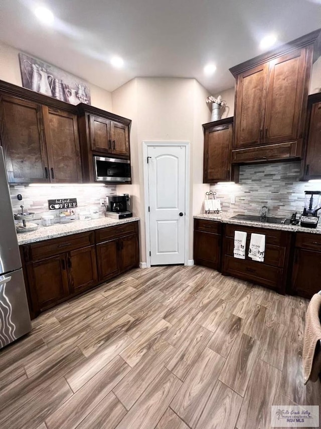 kitchen with appliances with stainless steel finishes, dark brown cabinetry, light stone counters, and decorative backsplash