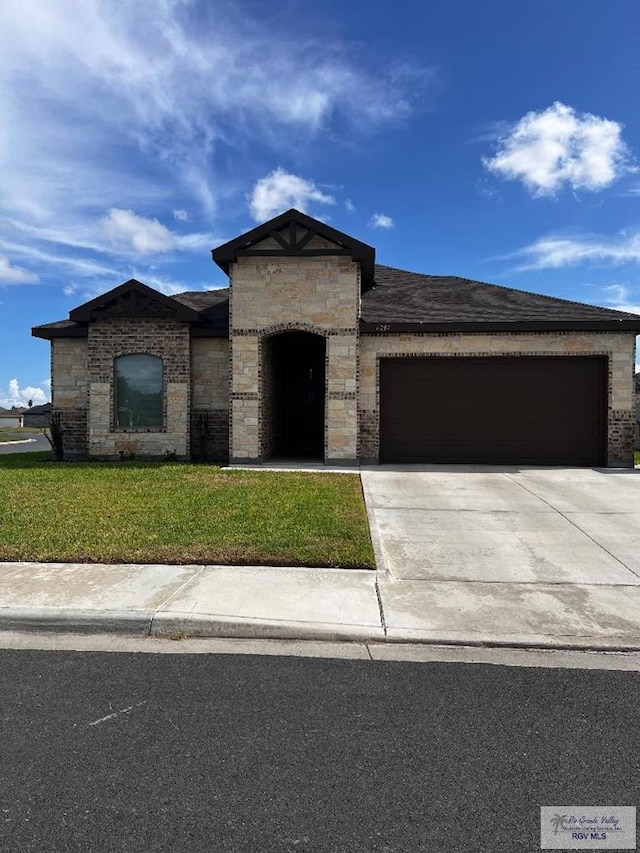 view of front of property with a garage, stone siding, driveway, and a front yard