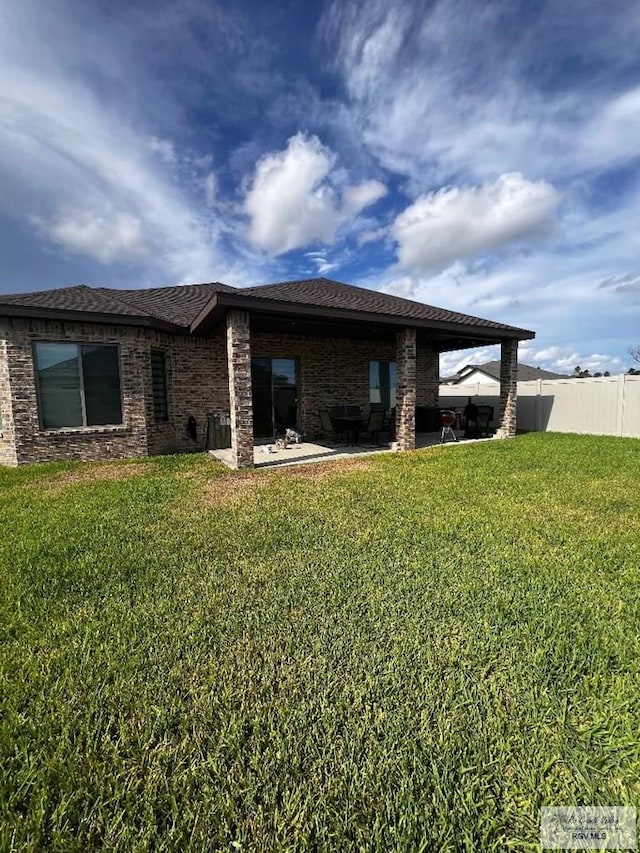 rear view of property featuring a patio, a lawn, and fence