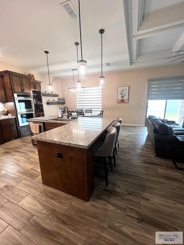 kitchen featuring a breakfast bar, visible vents, stainless steel double oven, a sink, and a large island with sink