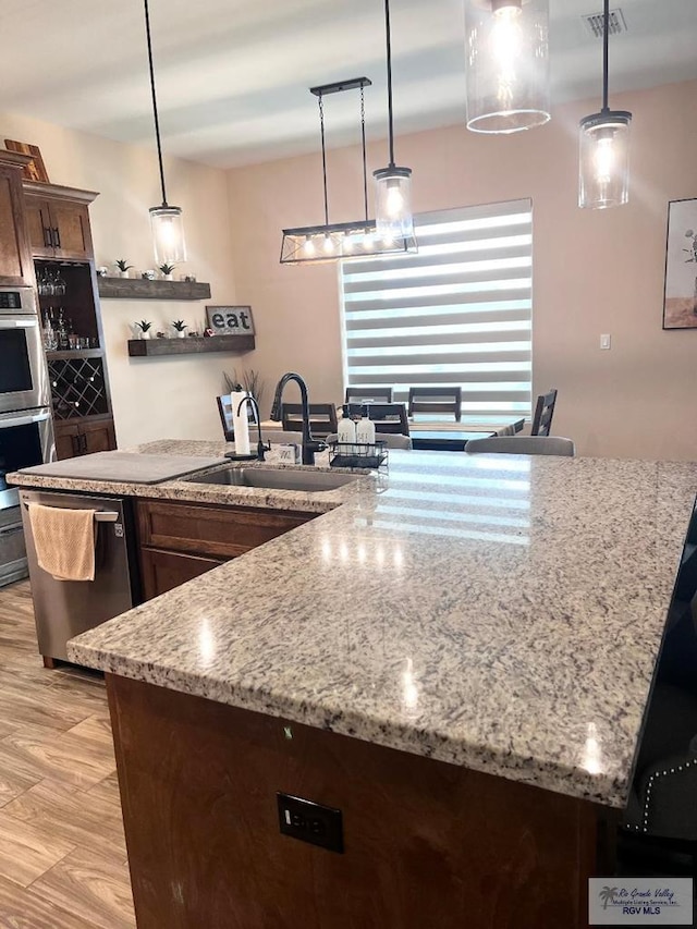 kitchen featuring light stone counters, decorative light fixtures, stainless steel appliances, light wood-style floors, and a sink