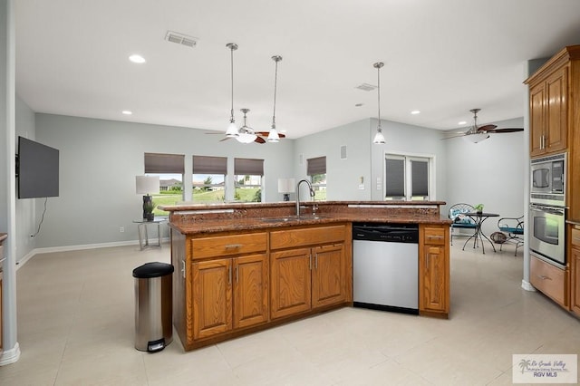 kitchen with appliances with stainless steel finishes, a kitchen island with sink, sink, stone countertops, and decorative light fixtures