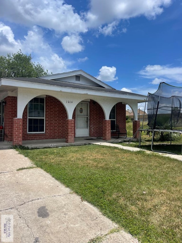 view of front facade featuring a trampoline, a front yard, brick siding, and a porch