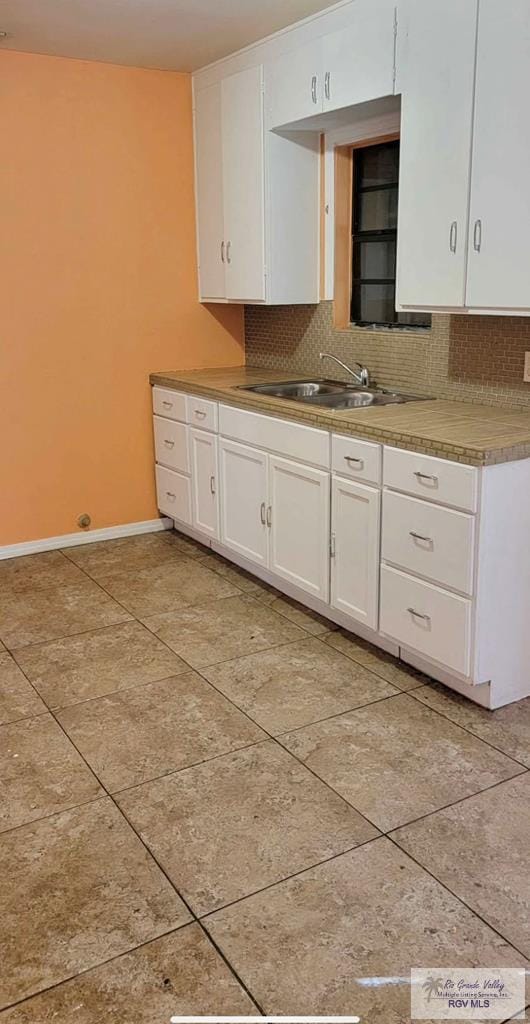 kitchen with light tile patterned flooring, sink, decorative backsplash, and white cabinets