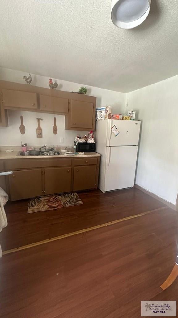 kitchen with a sink, a textured ceiling, freestanding refrigerator, black microwave, and dark wood-style flooring